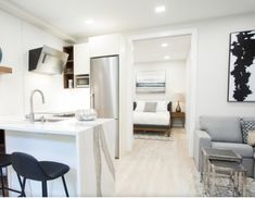 an open concept kitchen and living room with white walls, hardwood flooring and stainless steel appliances