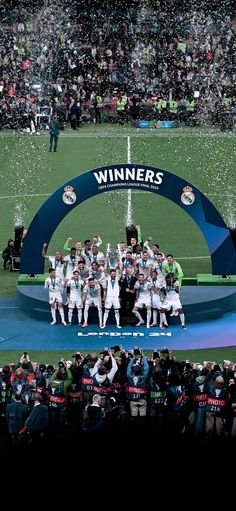 a group of men standing on top of a soccer field holding up a trophy while confetti is thrown in the air