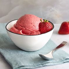 a bowl filled with ice cream next to two strawberries on top of a blue napkin