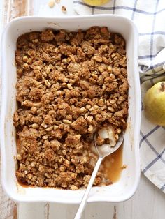 a white dish filled with apple crisp on top of a table next to pears