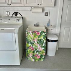 a white washer sitting next to a trash can in a room with white cabinets