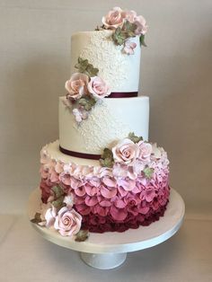 a three tiered wedding cake with pink and purple flowers on the top, sitting on a white pedestal