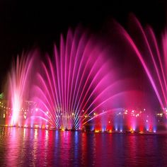 the colorful fountain show is lit up in pink and purple lights, reflecting on the water