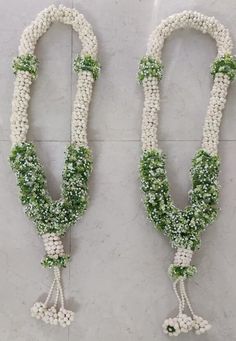 two white and green beaded necklaces with flowers on each strand, hanging from the wall