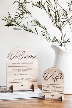 two wooden welcome signs sitting on top of a table next to a vase with a plant in it