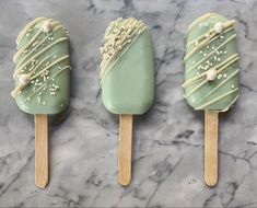 three popsicles with green frosting and sprinkles on them sitting on a marble surface