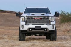 the front end of a white gmc truck parked in a field with dry grass