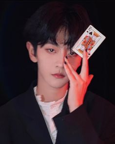 a young man holding up a playing card in front of his face with both hands