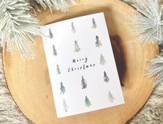 a christmas card sitting on top of a piece of wood next to some pine trees