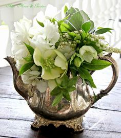 a silver vase with white flowers and greenery in it sitting on a wooden table