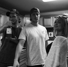 black and white photograph of three people standing in a kitchen with one holding a bottle