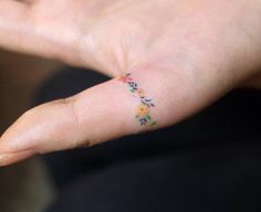 a person's hand with a small flower tattoo on their left thumb and finger