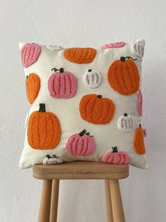 a white pillow with orange and pink pumpkins on it, sitting on a wooden stool