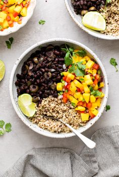 two bowls filled with black beans, mangoes and rice next to lime wedges