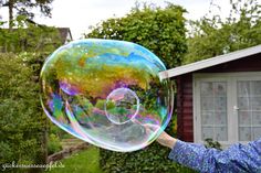 a woman holding up a bubble filled with water in front of a house and trees