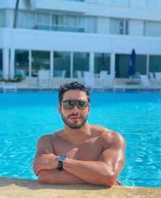 a shirtless man leaning on the edge of a swimming pool with his arms crossed