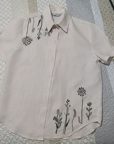 a white shirt with black flowers on it sitting on a quilted bed spreader