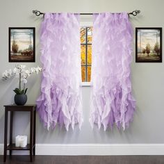 purple curtains hanging on the wall in front of a window with white flowers and framed pictures