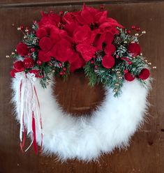 a wreath with poinsettis, pine cones and red flowers on it sitting on a wooden door