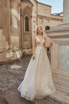 a woman standing in front of a building wearing a wedding dress and posing for the camera