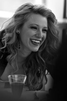 a woman sitting at a table with a glass in her hand and smiling for the camera