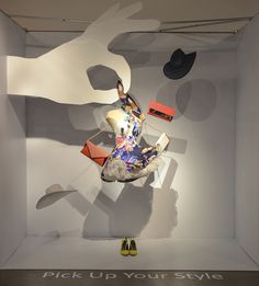 a display in a white box with shoes on the floor and an abstract painting behind it