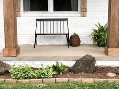 a bench sitting on top of a porch next to a white brick building with two windows