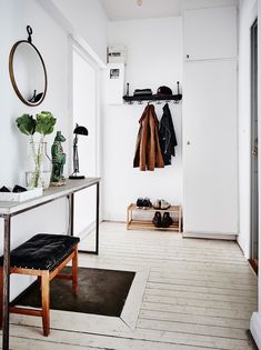 a white room with a coat rack and shoes on the floor next to a table