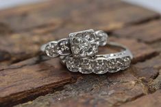 two wedding rings sitting on top of a wooden slab with stones in the background and one diamond set at the bottom