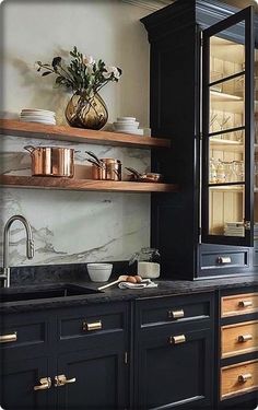 a kitchen with black cabinets and gold pulls on the countertop, along with copper pots and pans