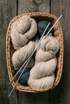 two skeins of yarn sit in a basket with knitting needles on the table