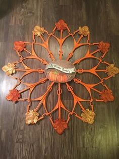 an orange metal clock on a wooden floor with leaves and scrolls around it's face