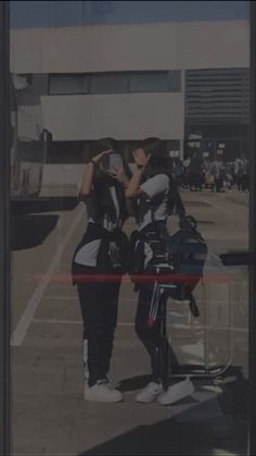 two women standing next to each other in front of a building taking pictures with their cell phones