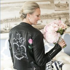 a woman in a white dress holding a bouquet of flowers and wearing a black leather jacket