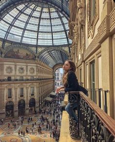 a woman standing on top of a balcony next to a glass ceiling filled with people