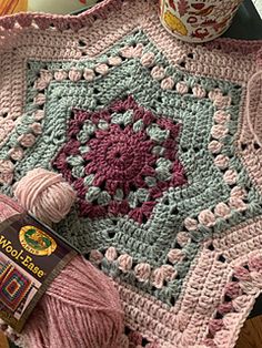 a crocheted blanket with yarn on it and a cup of coffee next to it