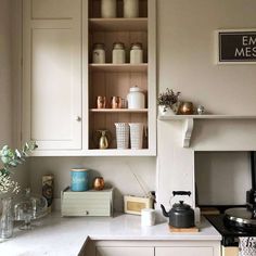 a kitchen with white cupboards and shelves filled with pots, pans and tea kettles