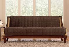 a brown futon couch sitting in front of a window on top of a carpeted floor