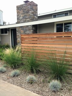 a wooden fence in front of a house with grass and bushes growing on the side