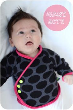 a baby laying on top of a bed wearing a black and pink shirt with polka dots