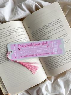 an open book with a tassel on top of it next to a pink bookmark