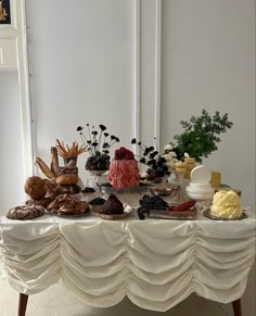 a table topped with lots of cakes and pastries on top of a white table cloth