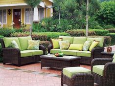 an outdoor patio with wicker furniture and green cushions on the floor, in front of a yellow house