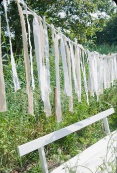 a white bench sitting in the grass next to a bunch of clothes hanging from a line