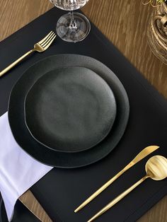 a place setting with black plates and gold utensils