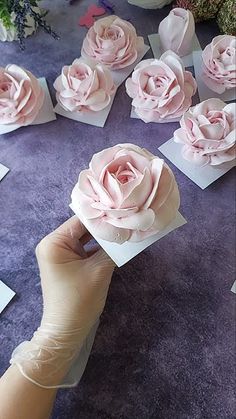 someone is holding some paper flowers in front of their face and hands, with other cards on the table