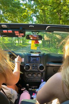 two women in the back seat of a car driving down a road with trees behind them