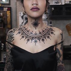 a woman with tattoos on her neck and chest is looking at the camera while wearing a black dress