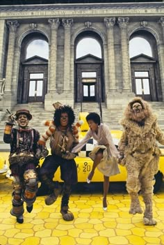 three people dressed in costumes standing next to a yellow car with two men on it