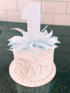 a white cake with a blue bow and the number one on it's top